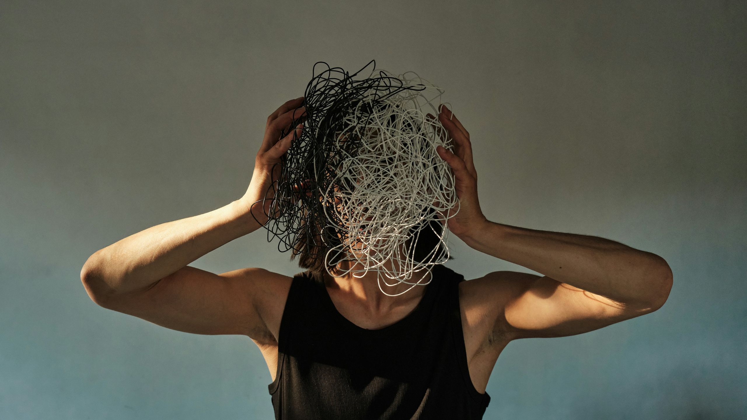 A man in a black vest holds white and black wire in a ball in front of his face representing creative burnout